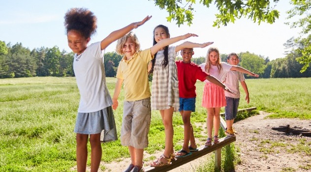 Bambini che giocano al parco camminando su una trave di legno mentre hanno le braccia allargate per non perdere l'equilibrio
