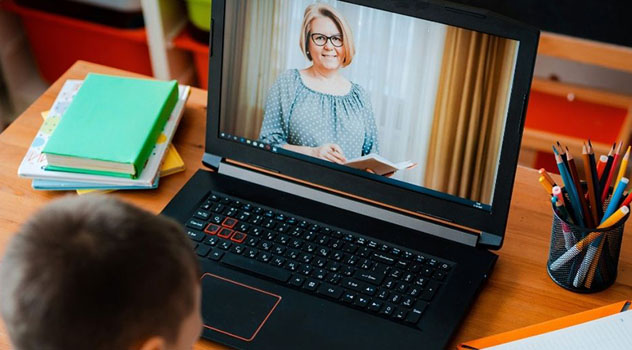 Un bambino davanti al pc che svolge la DAD mentre vede dal monitor la maestra che spiega la lezione.