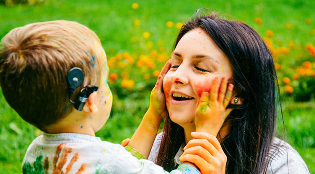 Bambino che indossa un impianto cocleare che gioca con i colori toccando la faccia della madre