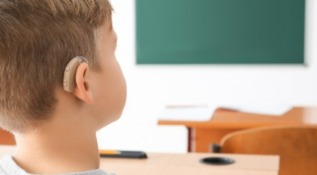 Bambino che indossa apparecchi acustici mentre segue una lezione a scuola.