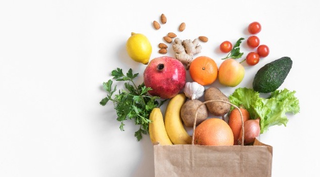 Busta della spesa con frutta e verdura che fuoriesce sullo sfondo bianco