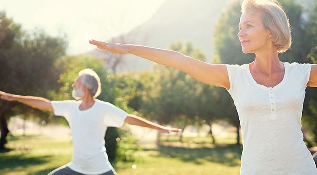 Coppia di adulti a braccia distese che pratica yoga in giardino