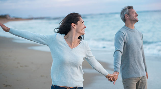 Coppia di adulti che sorridono e si tengono per mano in spiaggia in riva al mare