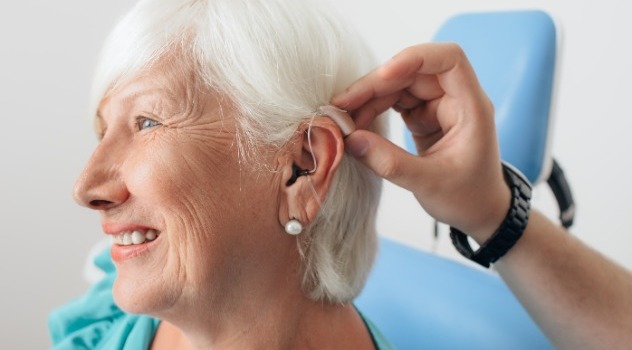Donna anziana sorridente che indossa un apparecchio acustico mentre la mano di un audioprotesista accende il dispositivo