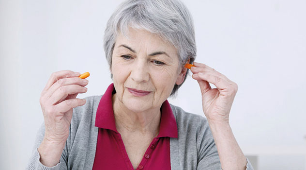 Donna anziana mentre si sta inserendo un tappo nell'orecchio sinistro e mantiene l'altro tappo con la mano destra