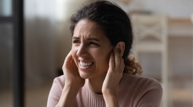 Giovane donna con una smorfia sofferente mentre si tappa le orecchie