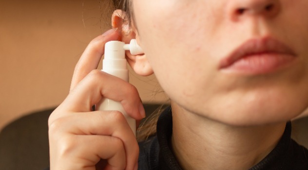 Una mano di una donna in primo piano mentre preme il dosatore di uno spray per pulirsi l'orecchio sinistro