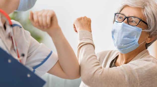 Professionista sanitario che saluta una paziente che indossa la mascherina con un colpo di gomito