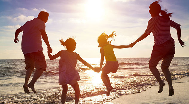 Una famiglia in riva mare al tramonto che si tiene per mano saltando tutti insieme