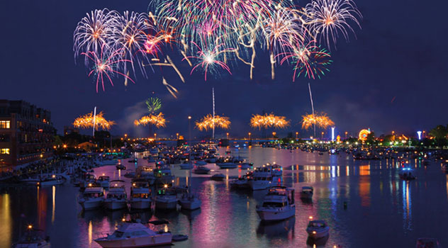 Fuochi d'artificio di color viola e arancione che esplodono in cielo sopra ad un fiume popolato di barche
