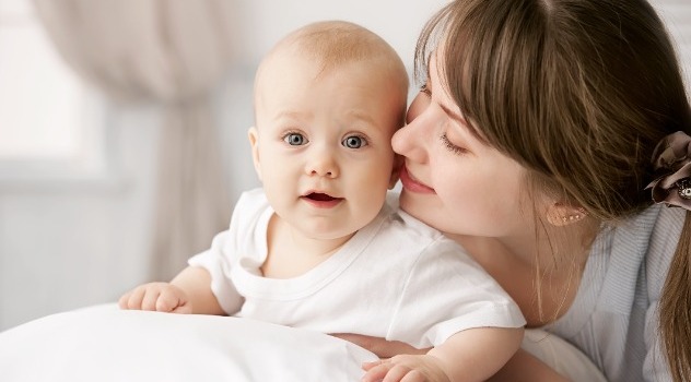 Giovane mamma che sorride e sussurra qualcosa all'orecchio del proprio figlio neonato