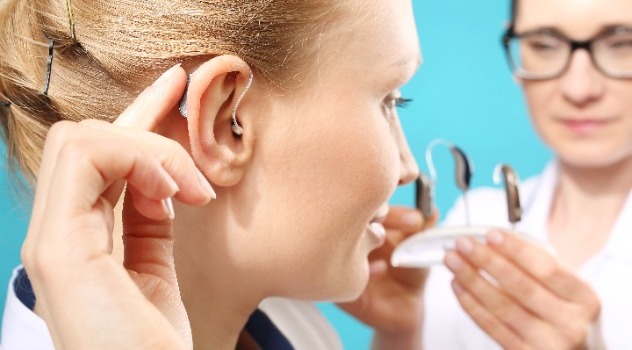 Giovane ragazza che indossa un apparecchio acustico mentre sullo sfondo l'audioprotesista le illustra varie scelte
