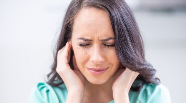 Giovane ragazza con sguardo sofferente e occhi chiusi che si tappa le orecchie