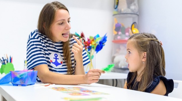 Logopedista mentre mostra ad una bambina il movimento della lingua per pronunciare una determinata parola