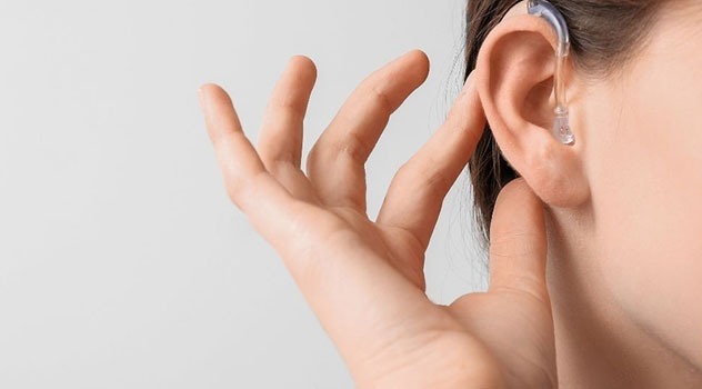 Primo piano di una mano femminile che preme sull'apparecchio acustico indossato all'orecchio.