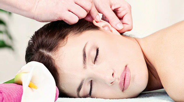 Il viso rilassato di una donna sdraiata sul lettino mentre sta ricevendo un massaggio auricolare