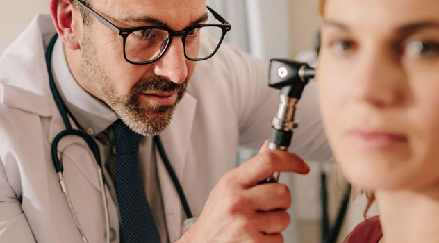 Otorino mentre esegue una visita all'orecchio di una paziente usando un otoscopio