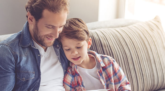 Padre e figlio seduti sul divano mentre hanno lo sguardo rivolto ad un libro