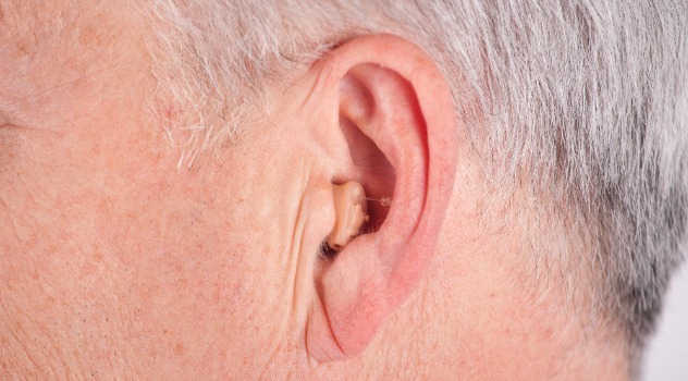 Primo piano del profilo di un orecchio di un signore anziano che indossa un apparecchio acustico endoauricolare