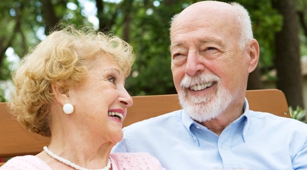 Primo piano di una donna con l'apparecchio acustico che sorride al marito mentre sono seduti su una panchina all'aperto