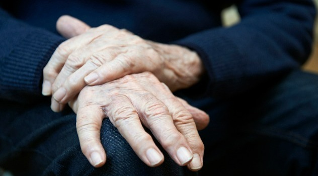 Primo piano di due mani tremolanti di un signore anziano affetto da Parkinson.