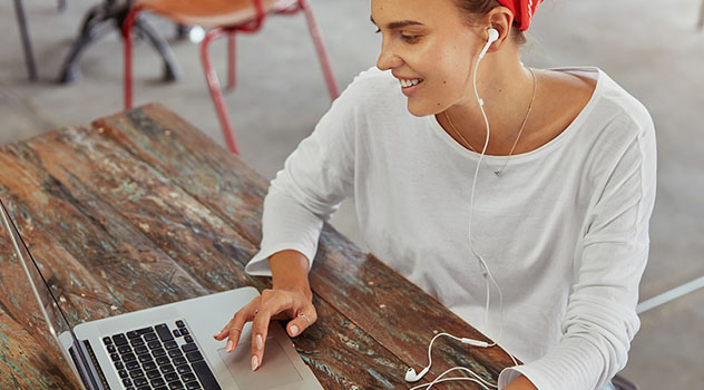 Una giovane ragazza seduta ad un tavolino mentre ascolta l'audio proveniente dal computer con un auricolare