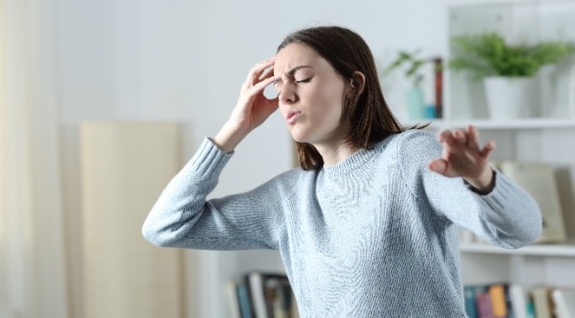 Ragazza con espressione sofferente durante un attacco di vertigine che si mantiene la tempia con la mano destra e allunga il braccio sinistro per ritrovare equilibrio