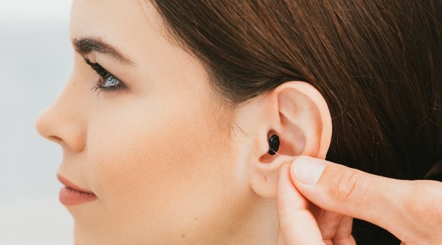 Profilo di una giovane ragazza mentre la mano di un audioprotesista inserisce un mini apparecchio acustico nel suo orecchio.