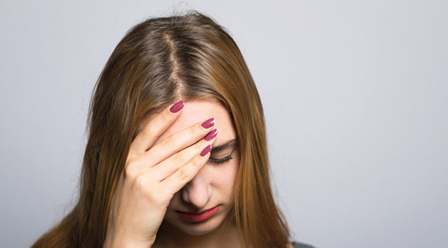 Primo piano del viso di una ragazza desolata con lo sguardo rivolto verso il basso e una mano in fronte