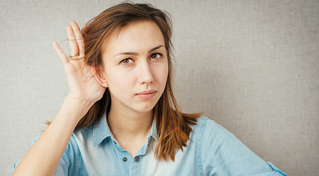 Una ragazza con la mano posizionata vicino all'orecchio per cercare di sentire meglio