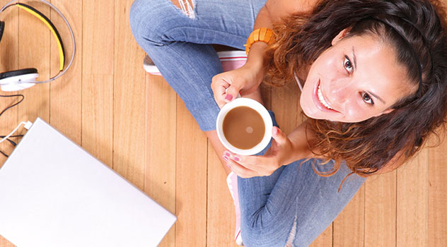 Immagine dall'alto di una ragazza sorridente con le gambe conserte mentre mantiene una tazza di caffè