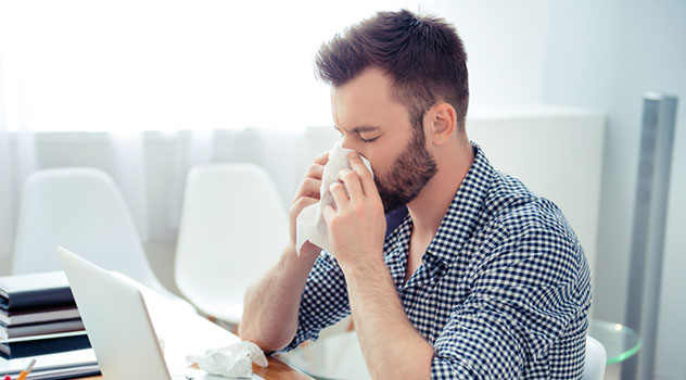 Ragazzo davanti al computer mentre si soffia il naso con un fazzoletto