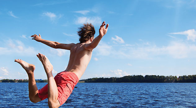 Ragazzo in costume mentre esegue un tuffo al mare con braccia e gambe divaricate