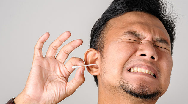 Uomo con la smorfia dolente mentre sta utilizzando il cotton fioc all'orecchio