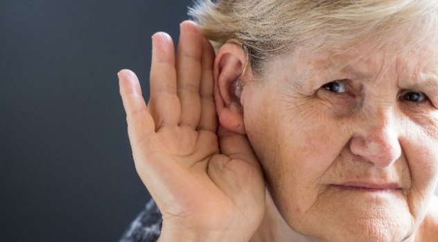 Una signora anziana che indossa un apparecchio acustico con la mano vicino all'orecchio per sentire meglio