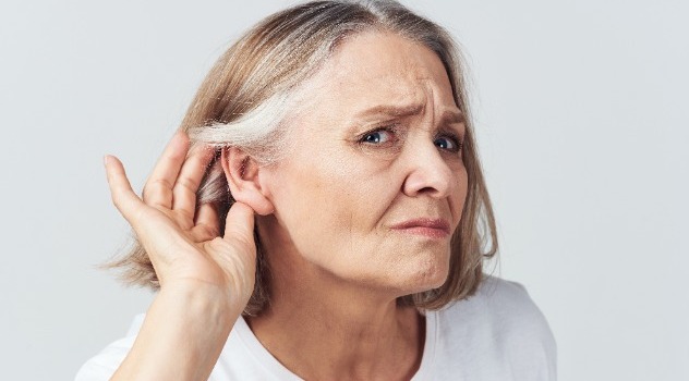 Una signora anziana con la mano vicino all'orecchio sinistro per sentire meglio