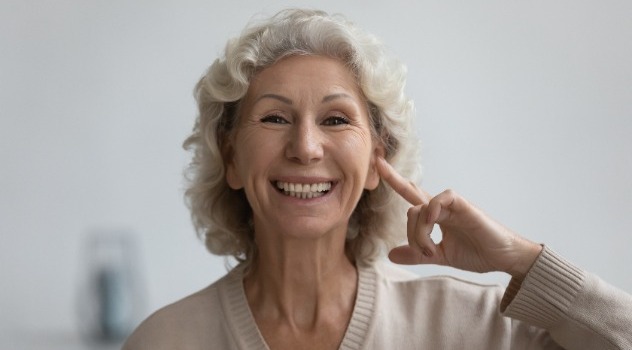 Signora anziana sorridente che indica il proprio orecchio sinistro