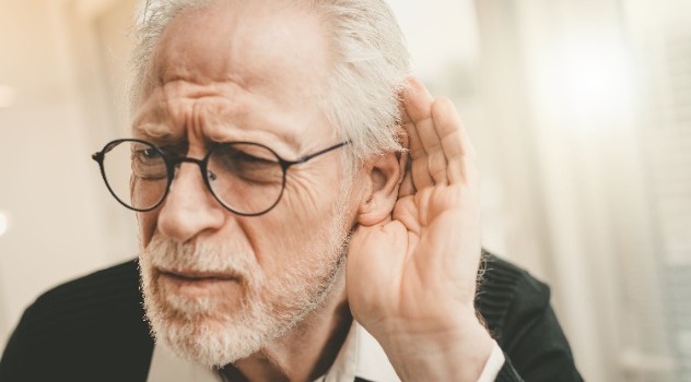 Un signore anziano con gli occhiali con la mano vicino all'orecchio per sentire meglio