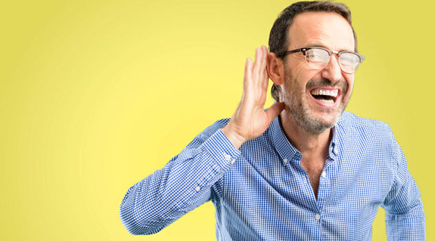 Un signore sorridente con camicia ed occhiali che ha la mano destra rivolta verso l'orecchio