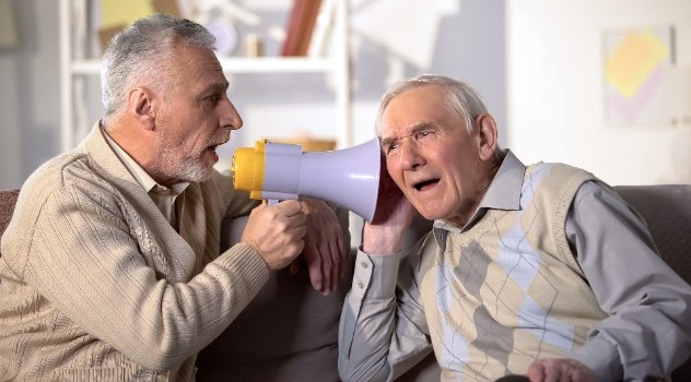 Un signore che parla con una persona anziana seduta vicino a lui sul divano usando il megafono in prossimità del suo orecchio