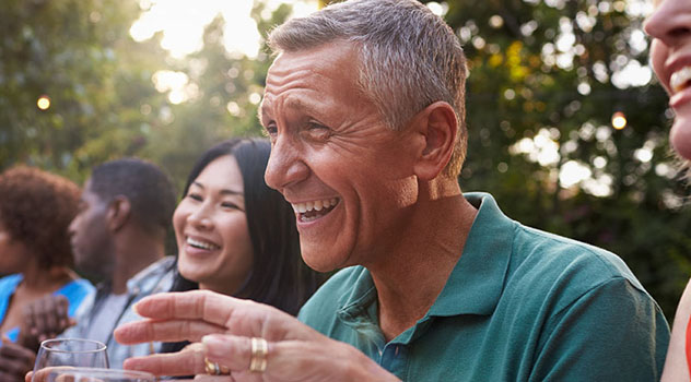 Un signore sorridente seduto ad un tavolino all'aperto in compagnia di altre persone sorridenti