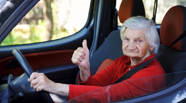 Simpatica signora anziana al volante mentre alza il pollice in senso di approvazione