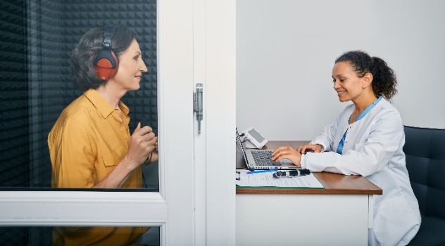 Una tecnica audioprotesista che controlla i risultati al computer mentre una paziente sta eseguendo un controllo dell'udito all'interno della cabina silente