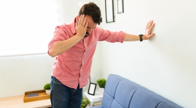 Uomo colto da un attacco di vertigine che si appoggia al muro per non cadere a terra e si tocca la tempia con la mano destra