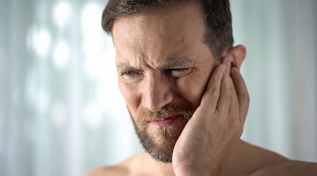 Un giovane uomo con la barba con espressione sofferente mentre si tocca l'orecchio sinistro dolorante