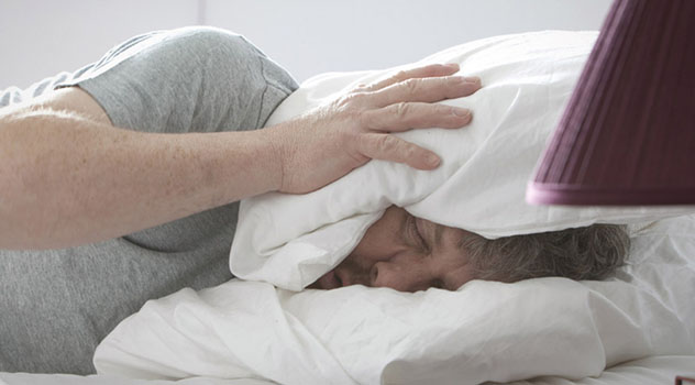 Uomo disteso sul letto con la testa avvolta nel cuscino per provare a dormire
