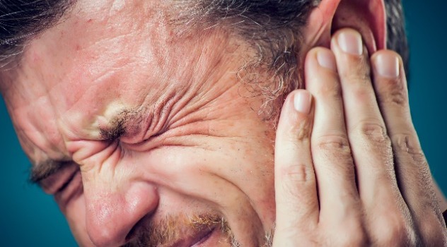 Primo piano di un uomo con espressione sofferente che si copre l'orecchio con la mano